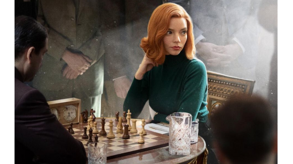 Beth Harmon (played by Anya Taylor-Joy) sitting in front of a chess board in a crowded, atmospheric room